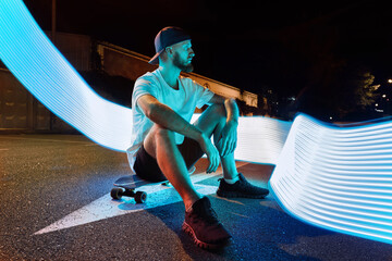 Man with skateboard on street with neon light