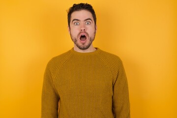 Wall Mural - Oh my God. Surprised Young man wearing casual sweater and over isolated yellow background  stares at camera with shocked expression exclaims with unexpectedness,