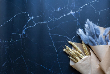 two bouquets of dry flowers on black marble background. template with dry flowers. Yellow wheat and blue lagurus on marble background.