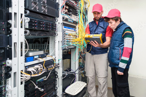 Two people work in a modern data center. Two specialists measure the signal level in the fiber optic cable. Serving a central router in a server room.