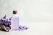 Bottle of essential oil and lavender flowers on light stone table. Space for text