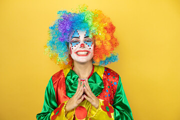 Clown standing over yellow insolated yellow background with Hands together and fingers crossed smiling relaxed and cheerful. Success and optimistic