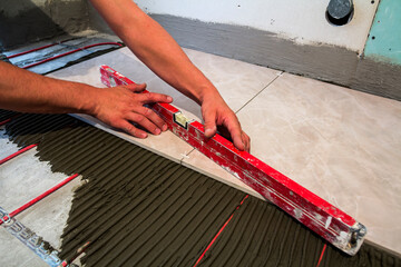 Canvas Print - Ceramic tiles and tools for tiler. Worker hand installing floor tiles. Home improvement, renovation - ceramic tile floor adhesive, mortar, level.