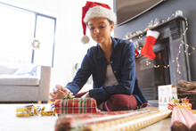 Woman In Santa Hat Wrapping Christmas Presents At Home