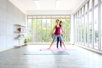 asian female yoga trainer helping her trainees stretching making tilts to the side before practice ,