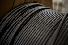 Vertical Coils Ndustrial Wires. Many Turns Of Main Electrical Cable Is Closeup. Roll Of Outdoor Fiber Optic Signal Shielded Cables. Wooden Coils Of Powerful Black Telecommunications Wire