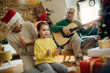 Joyful grandparents with granddaughter having fun on Christmas at home.