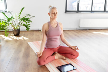 Canvas Print - mindfulness, spirituality and healthy lifestyle concept - woman with tablet pc computer meditating in lotus pose at yoga studio