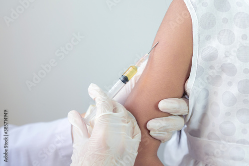 Female doctor or public health worker is injecting a flu treatment or a coronavirus or COVID-19 vaccine into the arm of an Asian child girl.