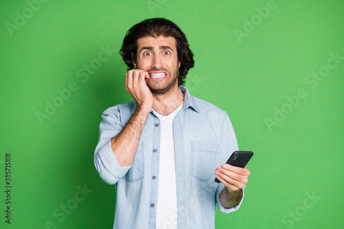 Portrait of his he nice attractive worried mature guy using gadget reading browsing post media news biting nails isolated over bright vivid shine vibrant green color background