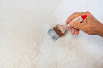 Hand of senior man hand with painted white on old wall in bathroom. Space for text. Renovation of the bathroom