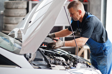 Car repair and maintenance theme. Mechanic in uniform working in auto service, checking engine.