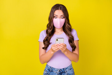 Sticker - Portrait of attractive stunned wavy-haired girl wearing safety mask using gadget blogging isolated over bright yellow color background