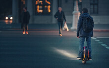 Man Riding Fast On Electric Unicycle Through Crosswalk At Night With Diode Lights. Mobile Portable Individual Transportation Vehicle. Night Riding, Man On Electric Mono-wheel Riding Fast (EUC)