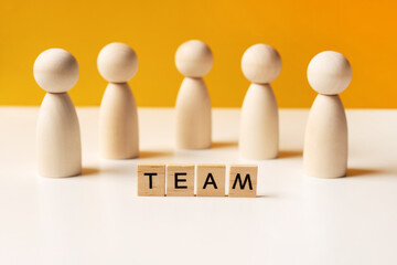 Company of wooden people on a yellow background with letters. The concept of team work and management, copy space