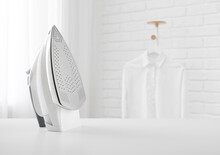 Electric Iron On Table In Blurred Room With Clothes Rack