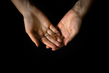 Female hands holding a brown wooden crucifix on a black blur background.The concept of religion Christianity or Catholicism.