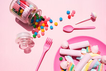 Studio Shot Of Plastic Plate Filled With Various Sweets And Candies Spilling Out From Toppled Jar