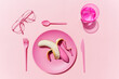 © gemma ferrando & jeremie roman/Westend61 - Studio shot of pink plastic tableware, glass of water, eyeglasses and pink peeled banana
