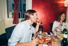 Young Man Eating Pizza During Social Gathering At Home