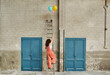 © victor espadas gonzalez/Westend61 - Woman climbing ladder leaning on wall while reaching for colorful helium balloons