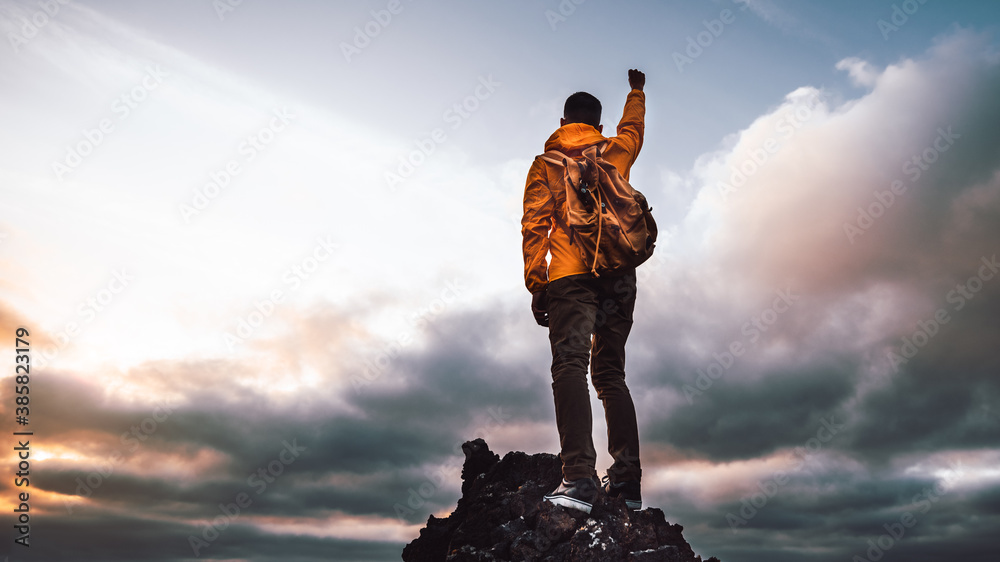 Hiker standing on the cliff mountain pointing the sky with fingers at sunset. Successful man on the top of the mountains. - obrazy, fototapety, plakaty 