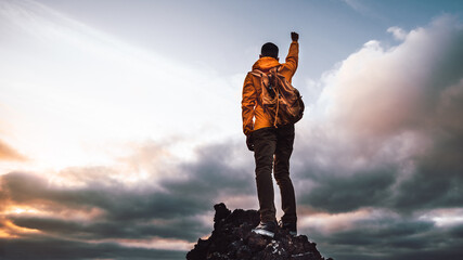 Wall Mural - Hiker standing on the cliff mountain pointing the sky with fingers at sunset. Successful man on the top of the mountains.