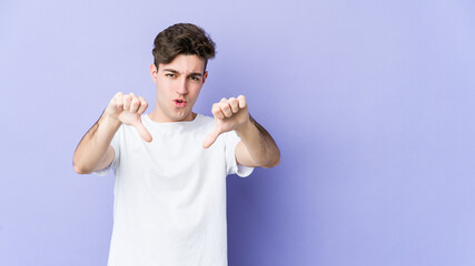 Wall Mural - Young caucasian man isolated on purple background showing thumb down and expressing dislike.