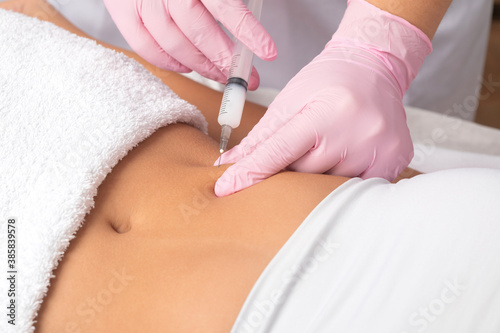 A doctor of aesthetic cosmetology makes lipolytic injections to burn body fat on a woman’s stomach and body. Female aesthetic cosmetology in a beauty salon.