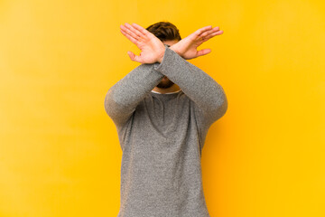 Wall Mural - Young caucasian man isolated on yellow background keeping two arms crossed, denial concept.