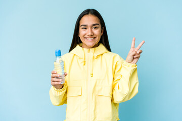 Young asian woman holding a bottle of water isolated on blue background showing number two with fingers.