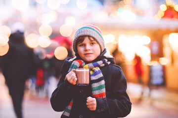 Wall Mural - Little cute kid boy drinking hot children punch or chocolate on German Christmas market. Happy child on traditional family market in Germany, Laughing boy in colorful winter clothes