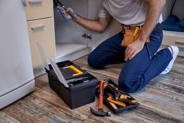 Wall Mural - Young worker fixing tubes under kitchen sink