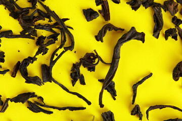 Wall Mural - Dry black loose tea leaves on yellow board, closeup detail from above