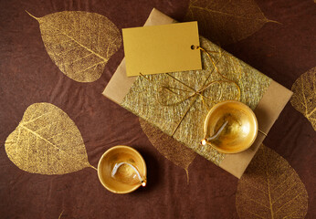 Glittering golden gift box with a blank tag and Indian traditional lamps. Diwali festive gift background. View from top.