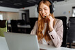 © Shopping King Louie - Smiling young female operator in headset works while sitting at the table, uses laptop, working in the call center.