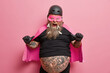 © wayhome.studio  - Pleased powerful man says look at me points at himself wears superhero costume has fun thick beard with clothespins isolated on pink studio background. Funny father entertains children on holiday