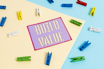 Poster - Handwriting text Build Value. Conceptual photo efficient enough way that it will generate profit after cost Colored clothespin paper empty reminder yellow blue floor background office