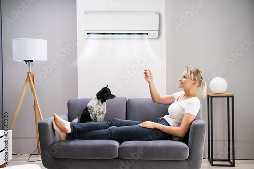 Happy Woman Sitting On Sofa Using Air Conditioner