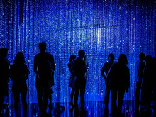 Silhouettes Of People Standing In Front Of Blue Led Light String