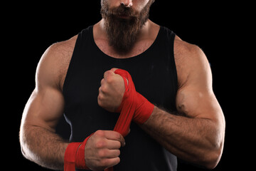 Wall Mural - Athlete stands in black clothes and wraps his hands in red textile elastic bandage before training.