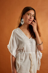 Young brunette Spanish woman dressed in white Ibizan style clothes, hat and straw bag on brown background 