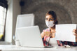 © Goran - Young businesswoman wears mask while having a video conference call with someone over the computer in the office