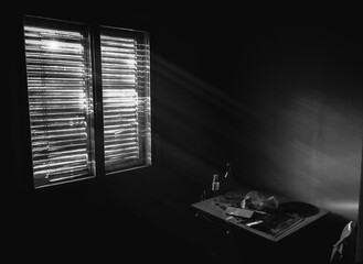 Dark small room in old apartment with wooden table and chairs near the window, sunlight coming through the blinds. Hard living background, depression and poverty concept. Black and white photography.