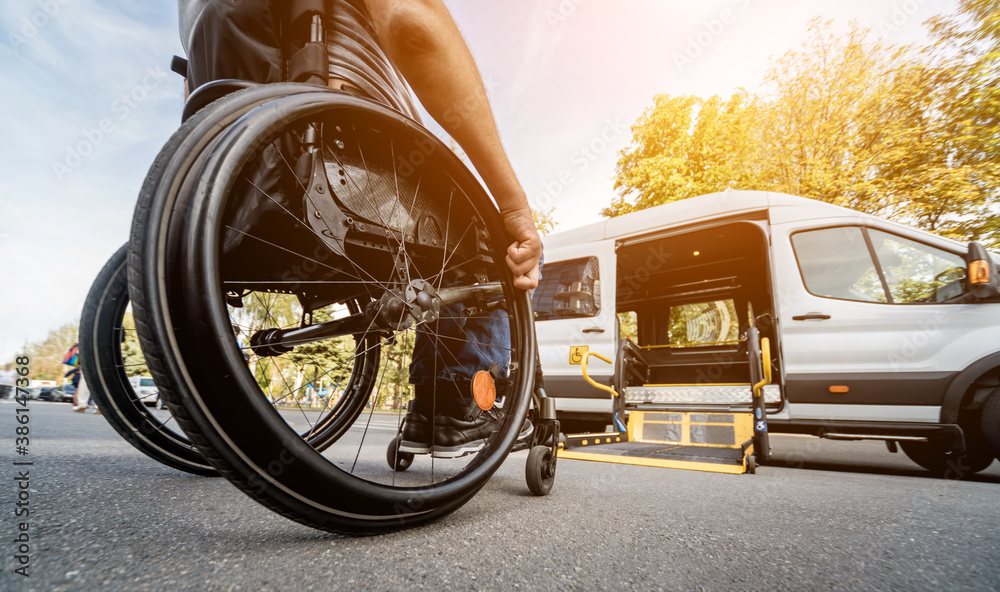 A man in a wheelchair moves to the lift of a specialized vehicle  - obrazy, fototapety, plakaty 