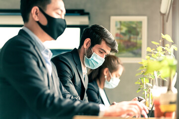 new normal lifestyle concept business people wearing mask sit with social distancing working in public area or co working space with laptop and smartphone