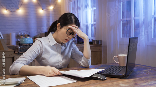 business people deadline stress and technology concept. young elegant businesswoman with laptop computer at night home office. worried lady in glasses holding lots of documents and feels depressed