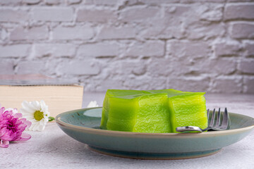 Layer sweet cake (or khanom Chan) on a plate with a book and flowers on gray stone background with white brick wall. Space for text. Selective focus. Relax time. Concept of dessert and relax time