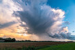 Anvil of a storm cloud is raining out over the dutch landscape at sunset