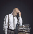 © stokkete - Pensive businessman leaning on a pile of paperwork
